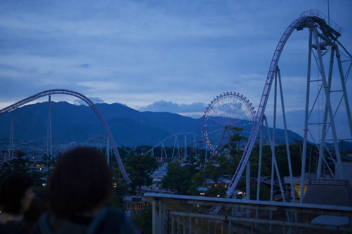 Roller coaster skyline of a Japanese amusement park at dusk with mountains behind