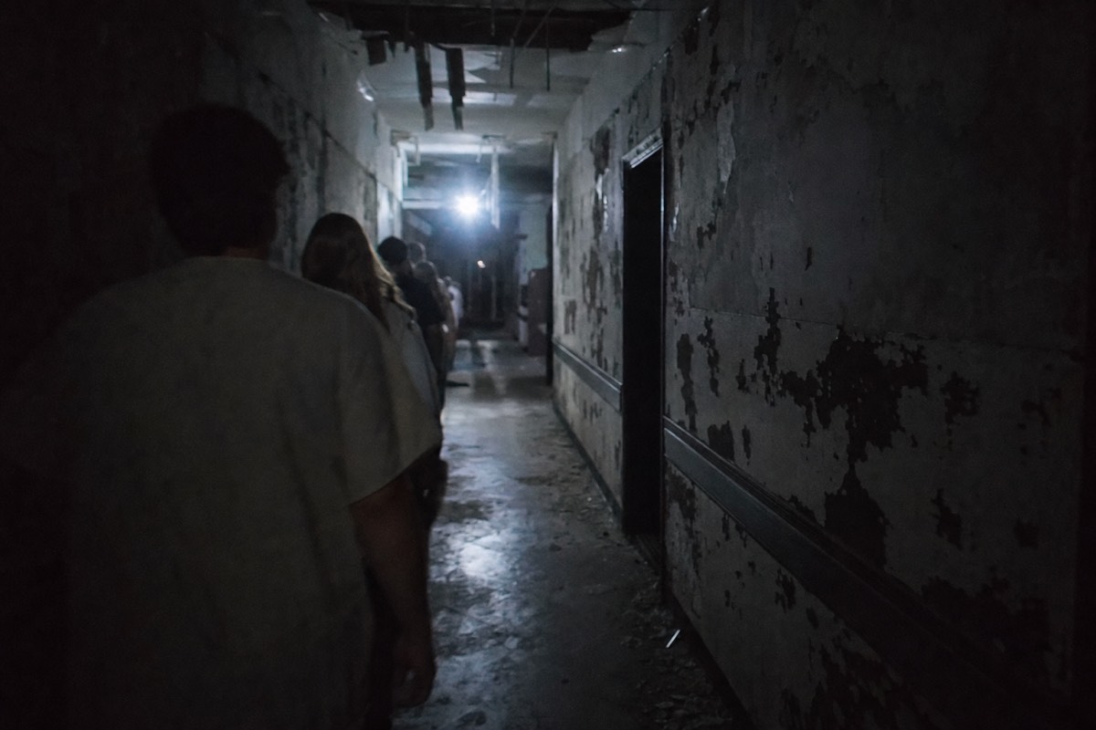Dim abandoned-hospital corridor of a walk-through horror attraction, flickering light at the far end