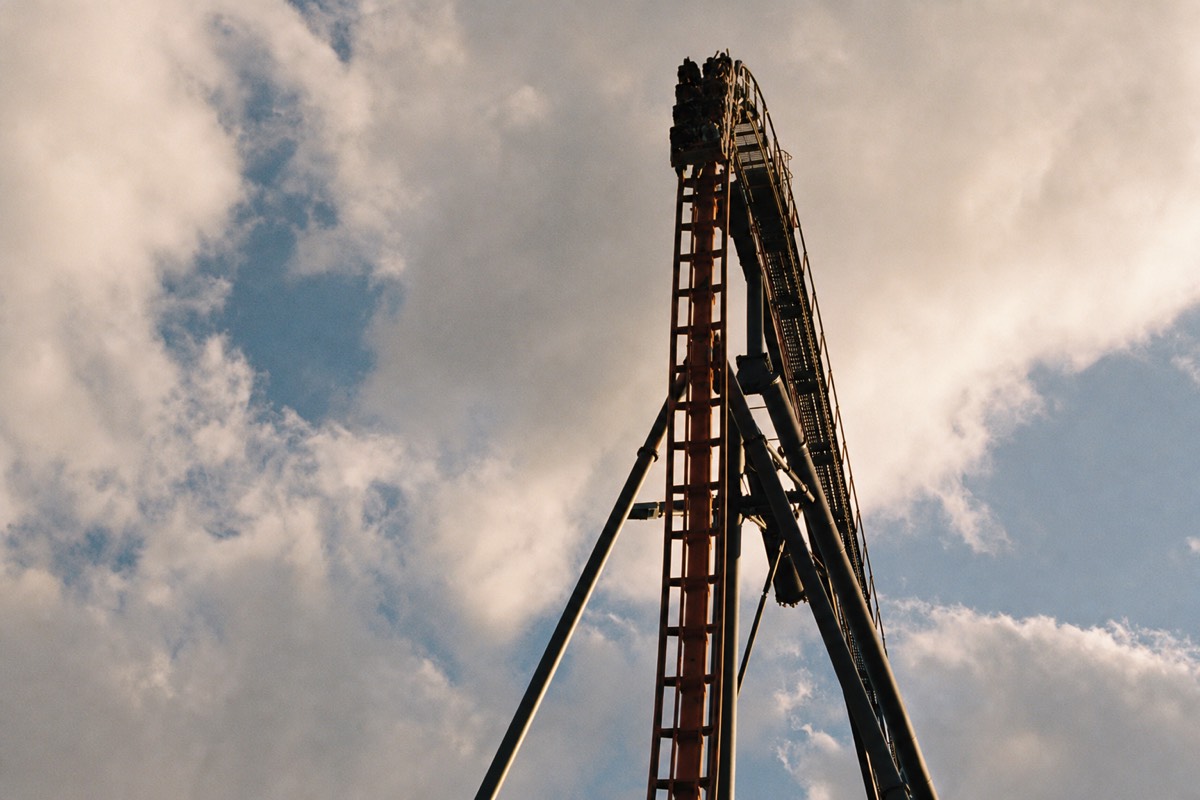 Beyond-vertical roller coaster drop against a clear sky, riders held at the crest