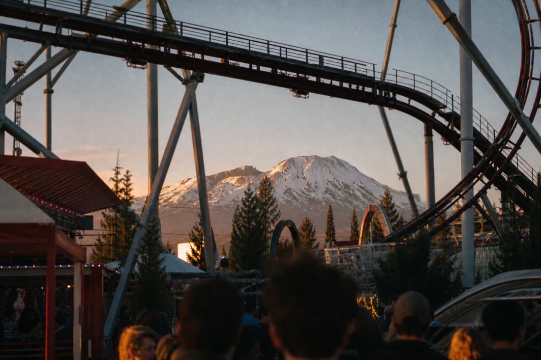 Amusement park midway under coaster structures with Mount Fuji beyond