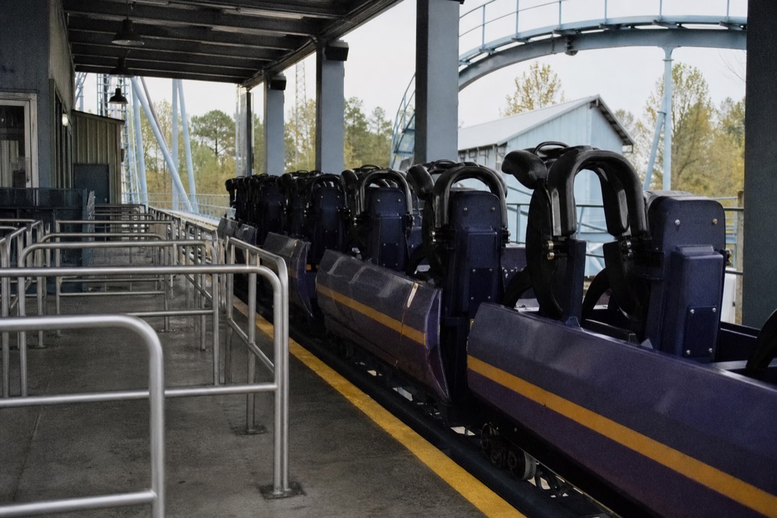 Single empty roller coaster train paused at a station platform beside quiet queue rails
