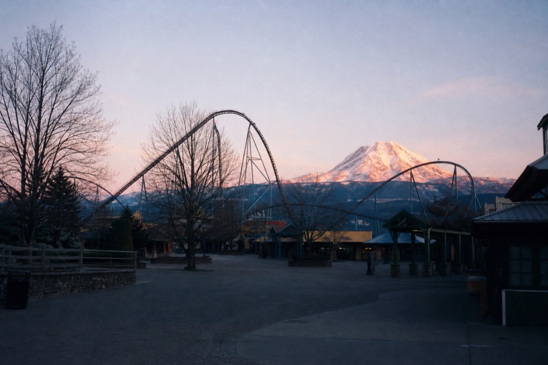 Early-morning theme-park plaza with roller coaster silhouettes and Mount Fuji catching first light before the crowds arrive